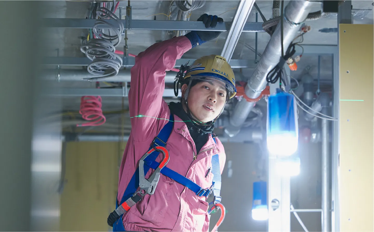 作業着を着た男性が天井のパイプを掴んで作業をする様子